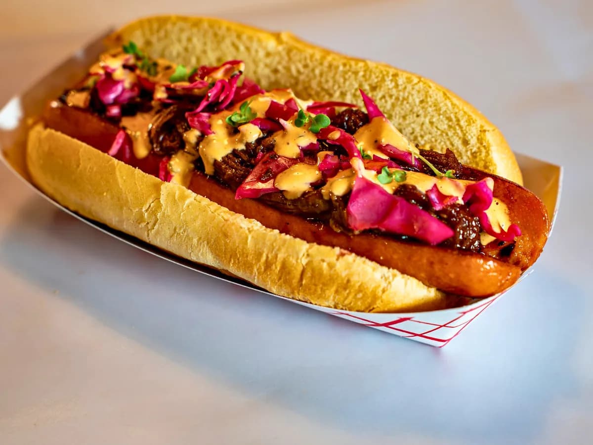 The Dam Dog, a split and griddled quarter-pound dog under pink pickled cabbage, in a paper boat.
