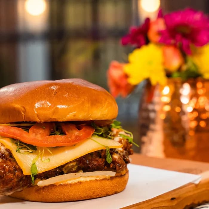 A recent post from The Burgerly’s Instagram — a chicken burger plated warm on a live-edge wood board.