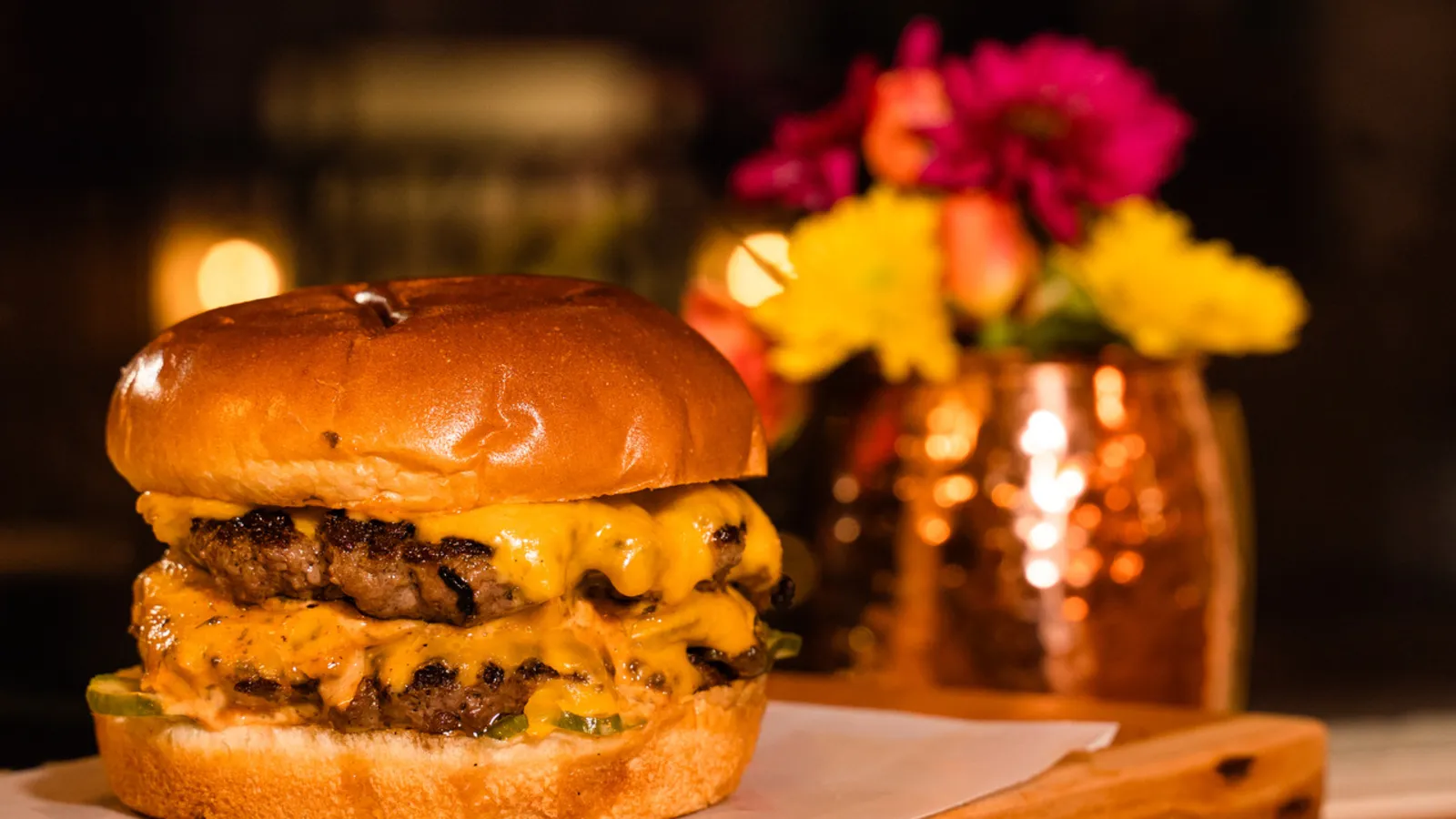 A chef-driven cheeseburger on a brioche bun with savory onions and house pickles, photographed warm on a live-edge wood board at The Burgerly in New Hope, PA.