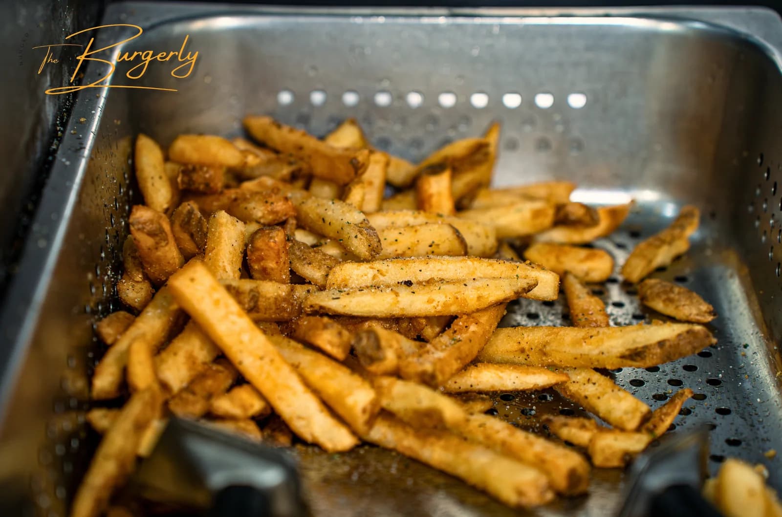Seasoned Fries — skin-on, double-fried, hand-cut potatoes finished with pink sea salt and an herbaceous house seasoning, in a stainless basket.
