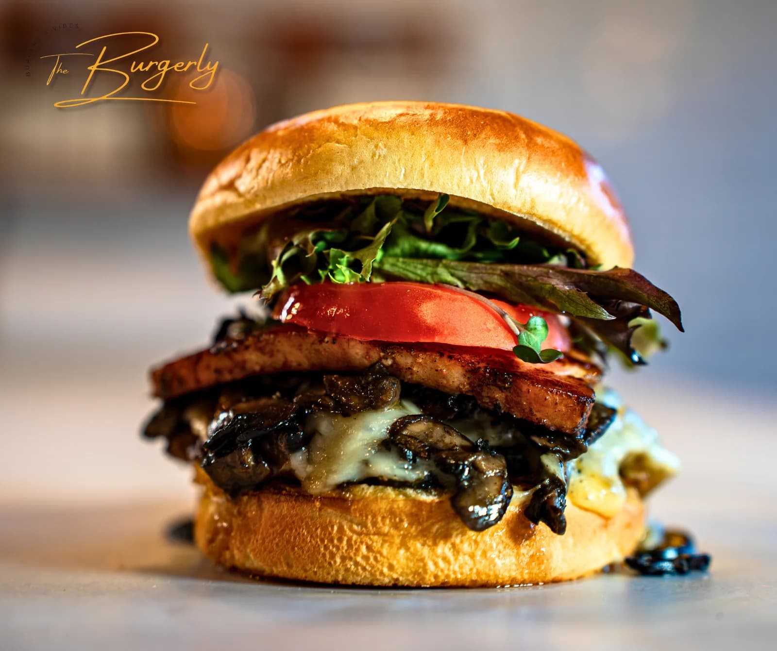 The Wonderful — a chef-driven brioche cheeseburger loaded with Havarti, house Canadian bacon, sautéed 'mazin mushrooms, fresh greens, and a thick tomato slice, photographed in close-up portrait.