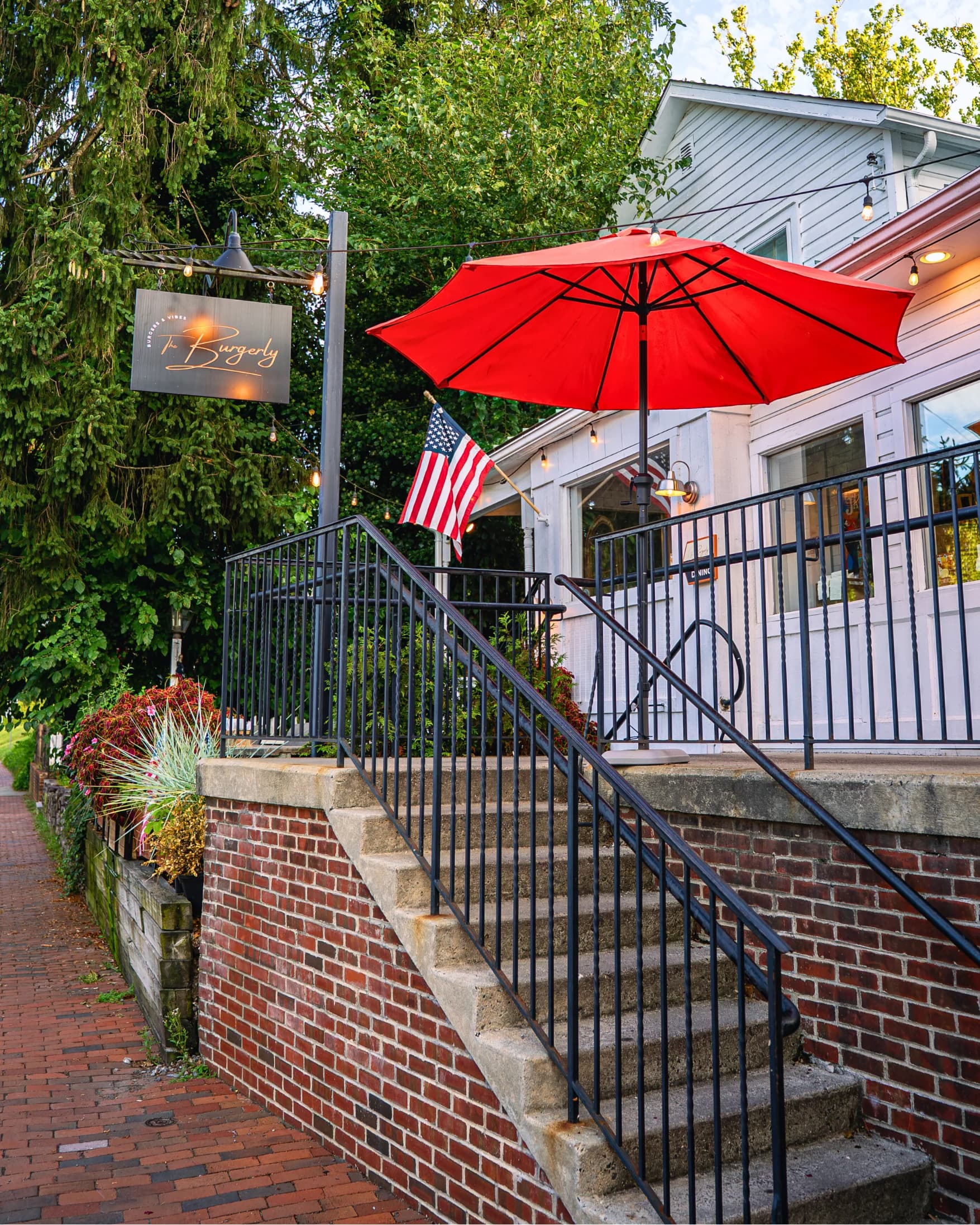 The Burgerly storefront at 137 S. Main Street, New Hope — white clapboard with red umbrellas, an American flag, the hanging copper Burgerly sign, and brick stairs leading up to the entrance, photographed at golden hour.